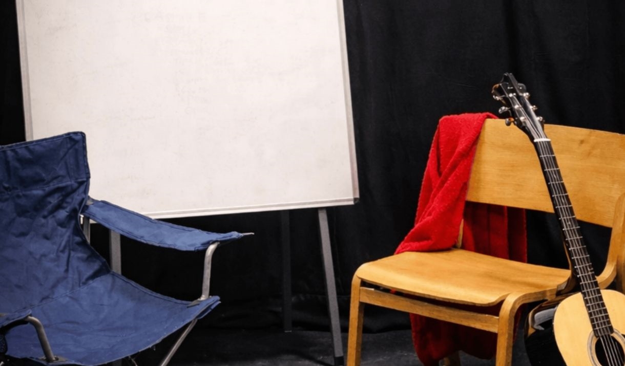 an room with two random chairs, an acoustic guitar, and a whiteboard. Sparkfest logo in top corner