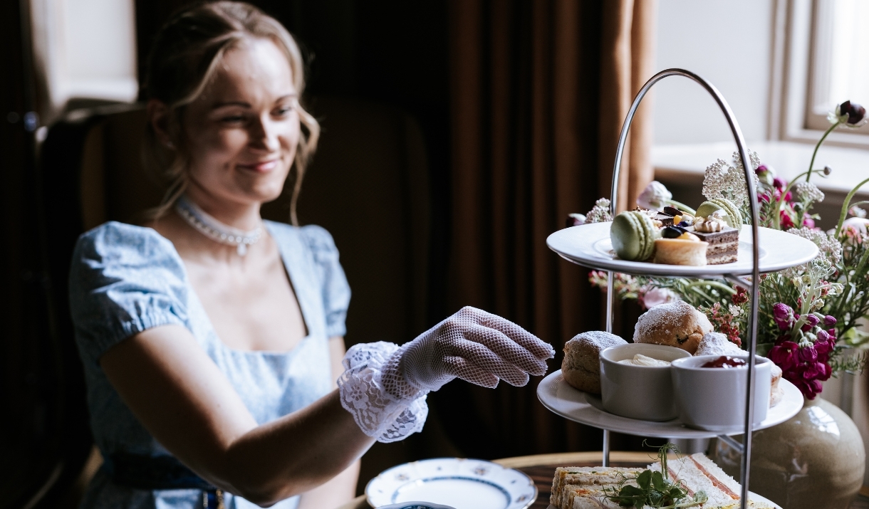 A woman dressed in period costume reaching towards a plate of scones