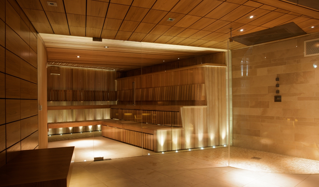 A large glass fronted sauna with wooden staged steps to sit on and low warm uplighters.