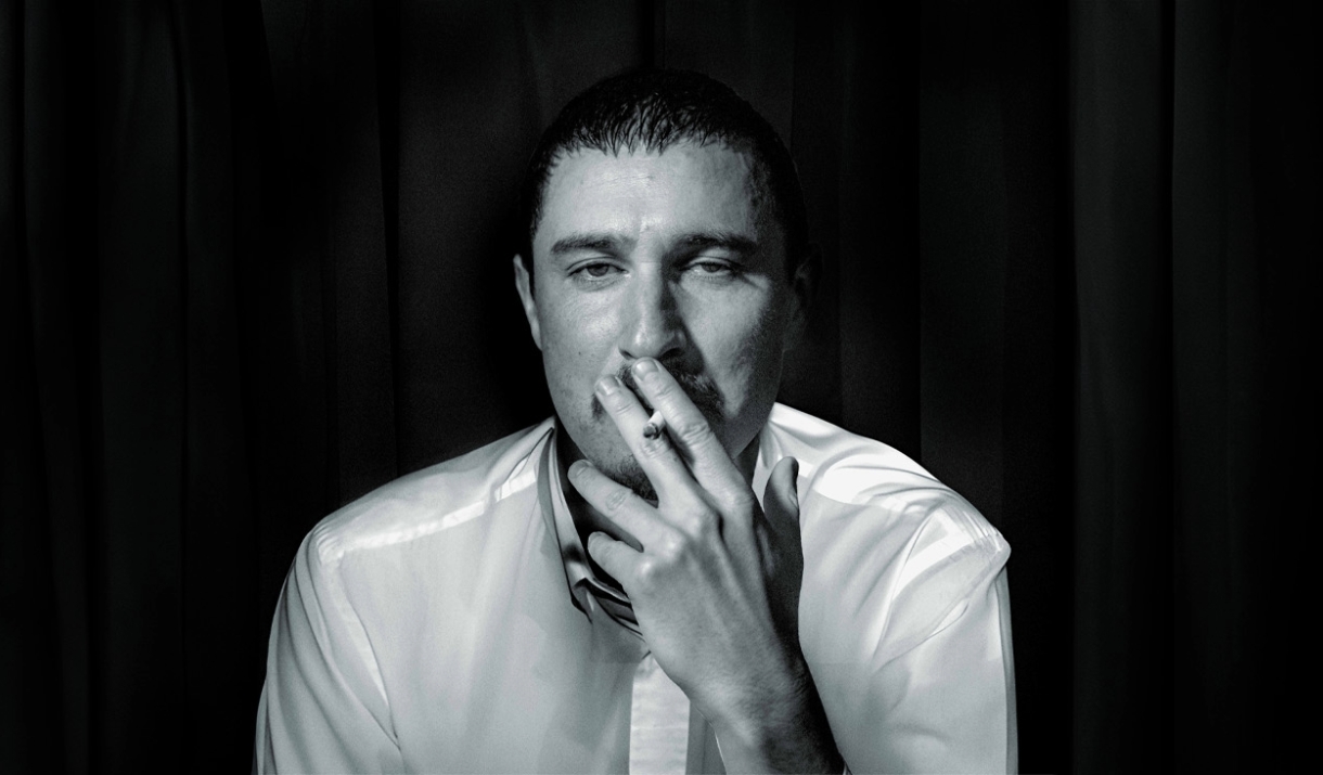 A black and white photo of the comedian Tom Rosenthal. He's smoking a Cigarette