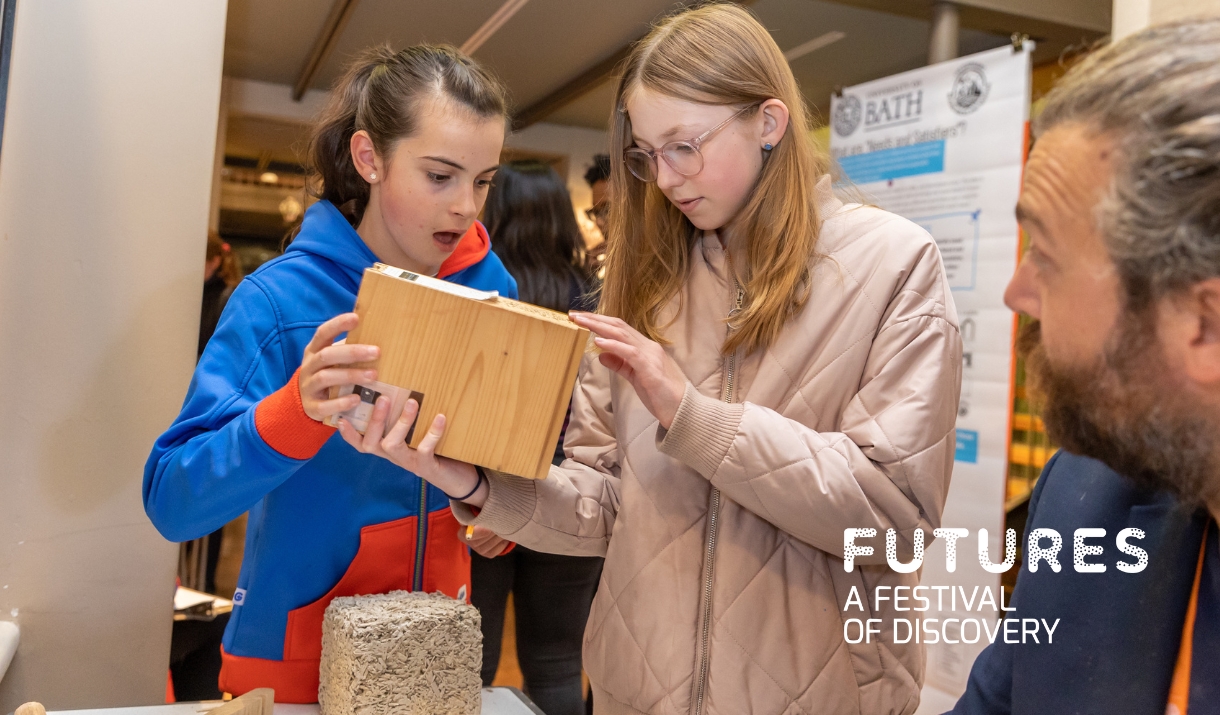Two young girls study some innovative building materials while a University of Bath researcher explains them