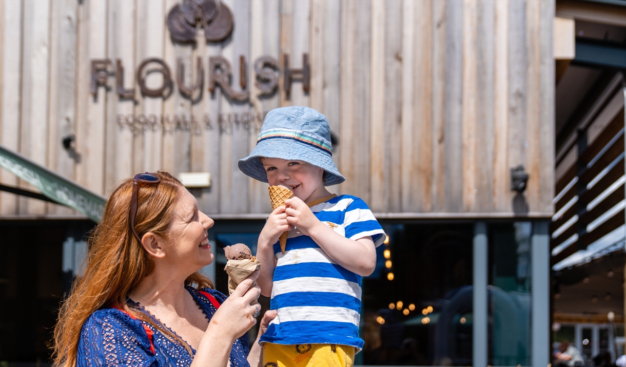 A woman with a child sitting on her shoulder. Both are eating ice creams.