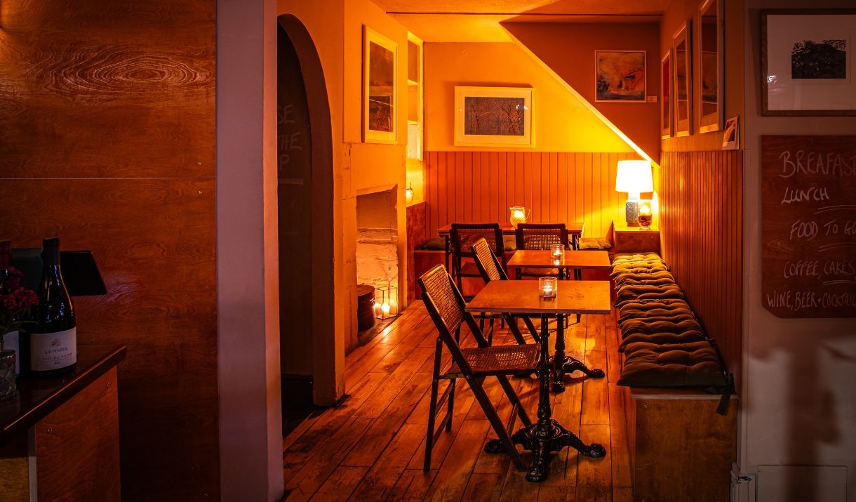 Multiple tables, chairs and a wall-length cushioned bench in a warmly-lit dining area