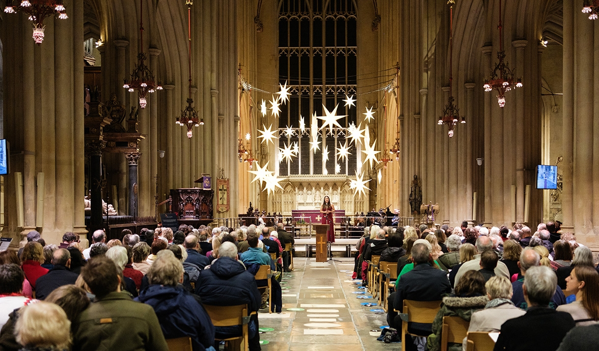 Photo of Chloe Jordan singing Christmas carol to audience sat in chairs inside of Bath Abbey in December as part of Wiltshire and Bath Air Ambulance C