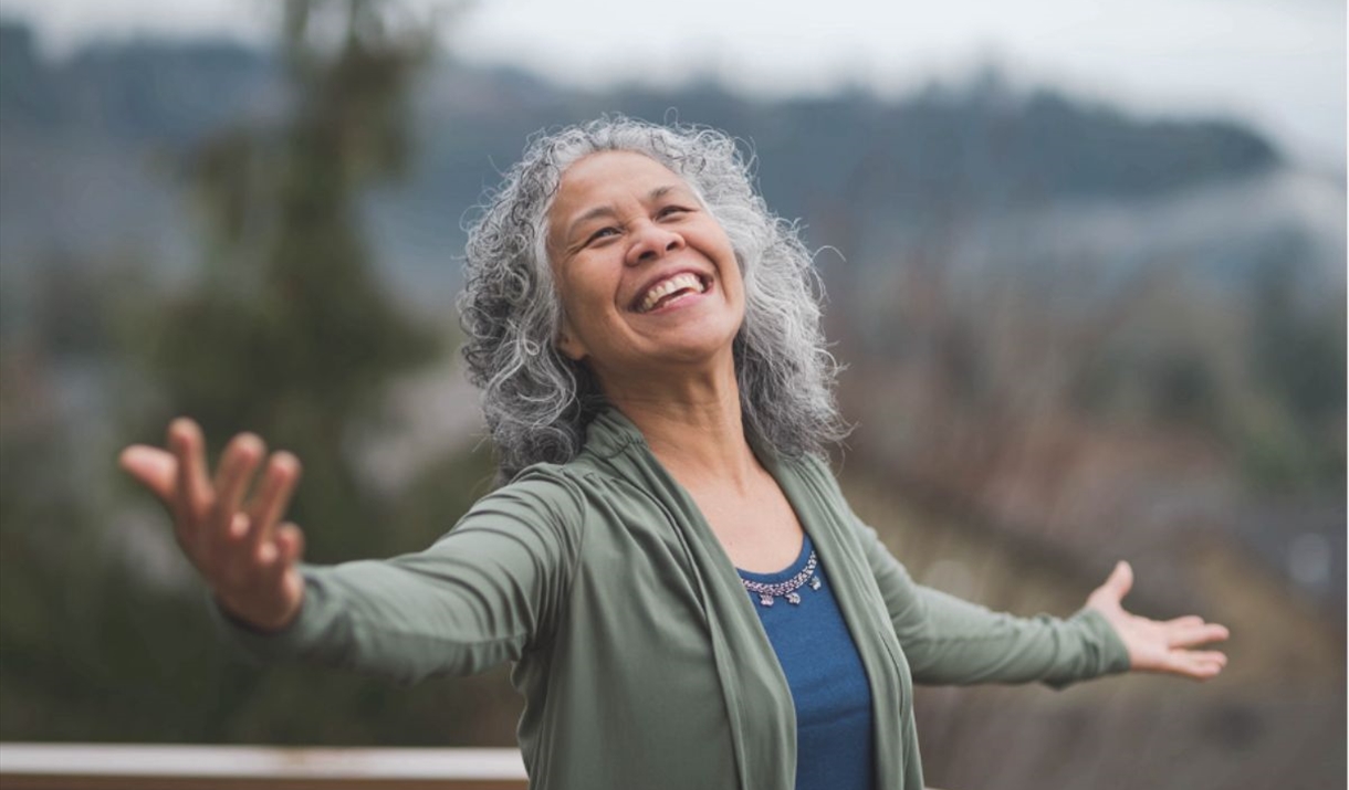 Happy older woman with arms open in nature