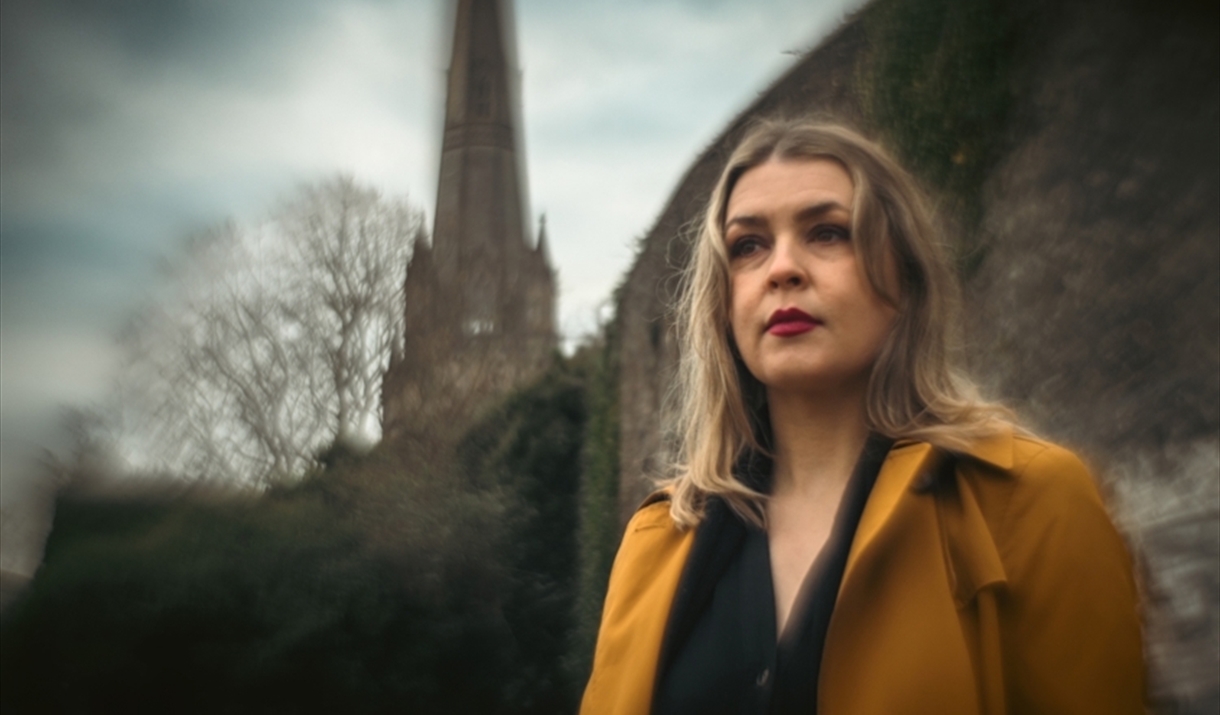 A woman in modern clothing, stood outside an old church.