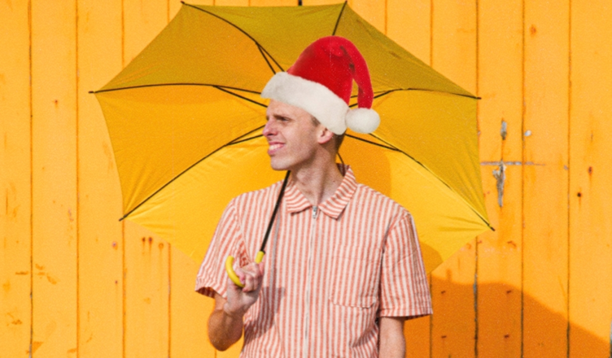 A man dressed in bright colours and a Santa hat holding a yellow umbrella