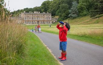 Boy looking through binoculars into parkland in front of a historic house