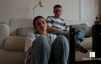 Two people. The male is sitting on a sofa and the female in front of him on the floor.