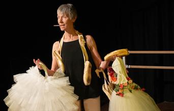 A woman in her 60's holding up ballet uniforms.