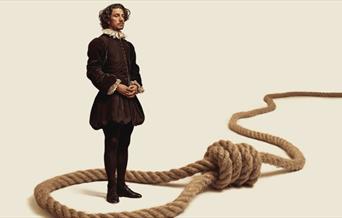 A man in 1500's attire stands in the middle of a loop with a running knot (noose).