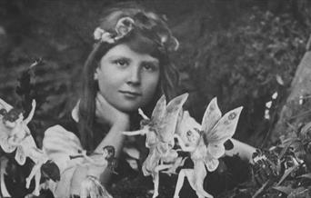 A black and white image of a child with long hair, with miniature fairies dancing around them.