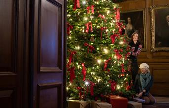 People decorating a large Christmas tree in a wooden panelled room