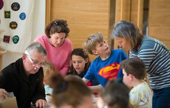 Photo of families around a table in a bright room, crafting together