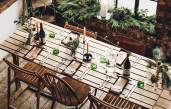 overhead shot of a beautiful bare brick warehouse space with a long table set for lunch and evergreens arranged on the large industrial window's sill