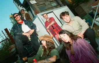 The Band posing on some stairs outside, strong mustaches and a cowboy hat