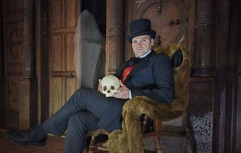 A man in victorian attire with a skull, a ghost is watching him