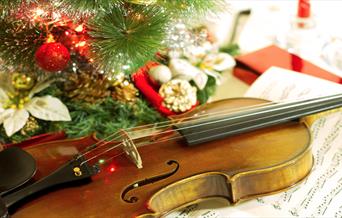 A violin surrounded by Christmas lights and ornaments