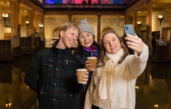 Three visitors enjoying a hot chocolate beside the Great Bath
