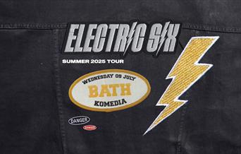 Jacket with patches: "Electric Six," "Summer 2025 Tour," "Wednesday 09 July BATH Komedia," and a lightning bolt and danger sign.