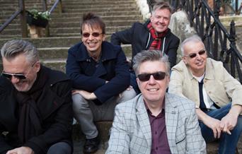 A group shot of The Undertones, all sitting on some steps, looking directly to camera