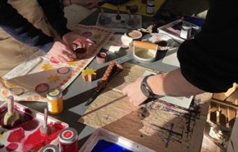two women stand on opposite sides of a craft table, block printing and lino printing at the Love Makers Craft Cafe in Bath