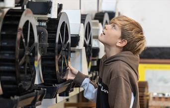 Boy looking at some large cogs on a machine at Saltford Brass Mill