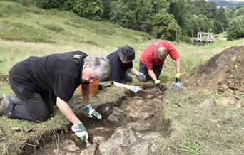 Volunteers digging in the Pasture uncovering stones from the Bason of Water with a view of Prior Park behind.