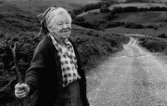 Black and white photograph of an elderly woman with a walking stick