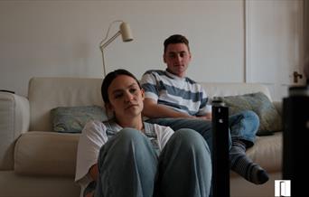 Two people. The male is sitting on a sofa and the female in front of him on the floor.