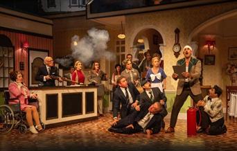 A scene from Fawlty Towers the play, containing most of the cast during a comedic moment.
