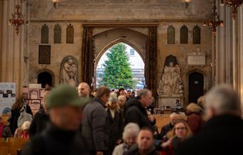 The open doors of a large church showing a Christmas tree outside, while people take their seats for a service inside