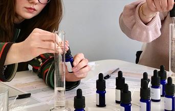 Perfume Making close, woman putting oil into a small blue jar