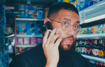 The comedian Jamail Maddix is talking on the phone while standing in a grocery store.