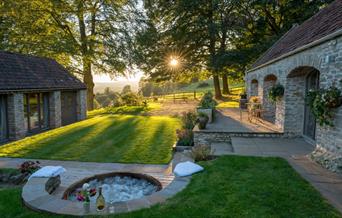 Scenic shot of a hot tub with champagne, the sunny countryside in the background, and the two brick lodgings.
