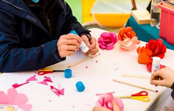 A crafting table with scissors, pencils and paper roses on.