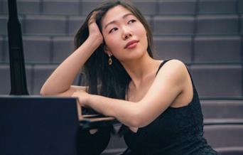 An image of Nurry Lee leaning on a piano.