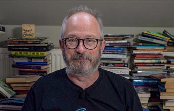 Robin Ince surrounded by stacks of books