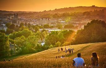 Scenic backdrop of people sitting on a hill in the late afternoon/early evening looking down at the city of Bath