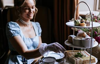 A woman eating afternoon tea while wearing period dress