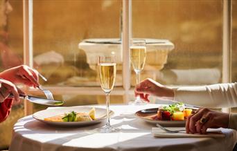 An image of two friends enjoying a delicious evening meal in the sunlit Pump Room