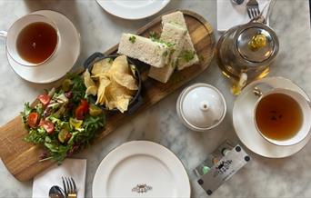 A sandwich, crisps and salad surrounded by tea and white crockery at The Abbey Tea Bar, Bath