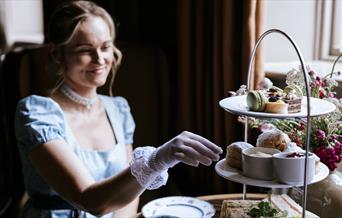 A woman dressed in period costume reaching towards a plate of scones