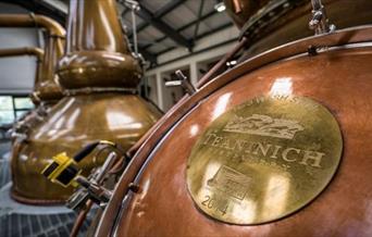 A close up image of the copper jacket of a whisky still. The distilleries name is engraved on the copper coloured hatch for the still. The distillery