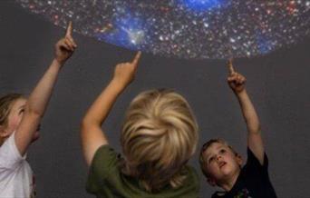 Three children pointing up at a planetarium display
