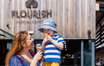 A woman with a child sitting on her shoulder. Both are eating ice creams.