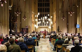 Photo of Chloe Jordan singing Christmas carol to audience sat in chairs inside of Bath Abbey in December as part of Wiltshire and Bath Air Ambulance C