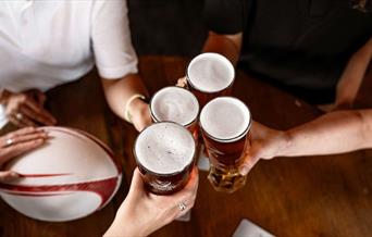 4 people cheersing a pint each, with a rugby ball on the table
