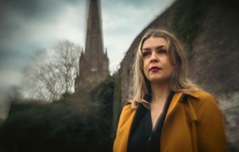 A woman in modern clothing, stood outside an old church.