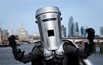 A photo of Count Binface - he has his fists raised up. In the Background is the London city skyline.